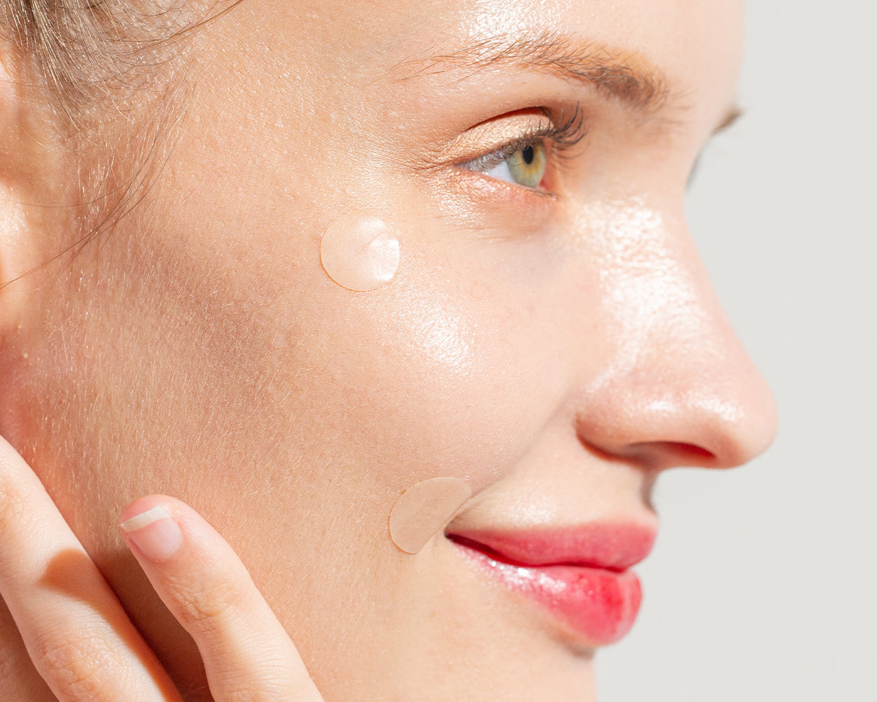Close-up of a woman's face showing skincare routine with an Avarelle GUNK OUT: Spot Tech 100CT acne patch on her cheek.