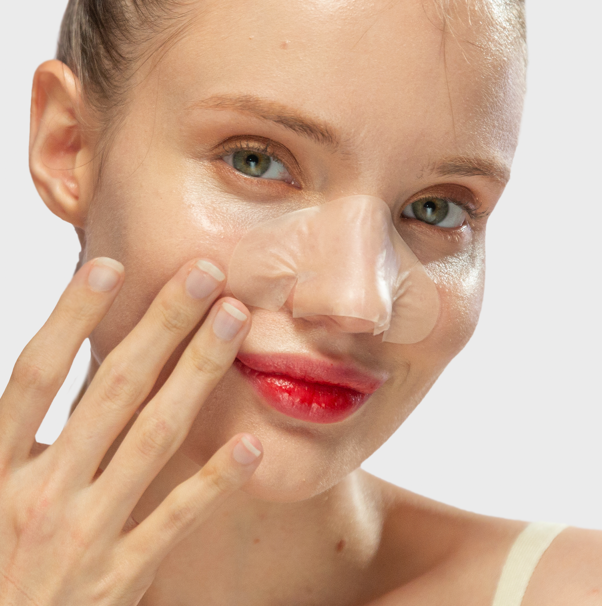 A woman with an Avarelle ZitOut Nose 16ct patch and red lipstick, touching her face and smiling slightly.